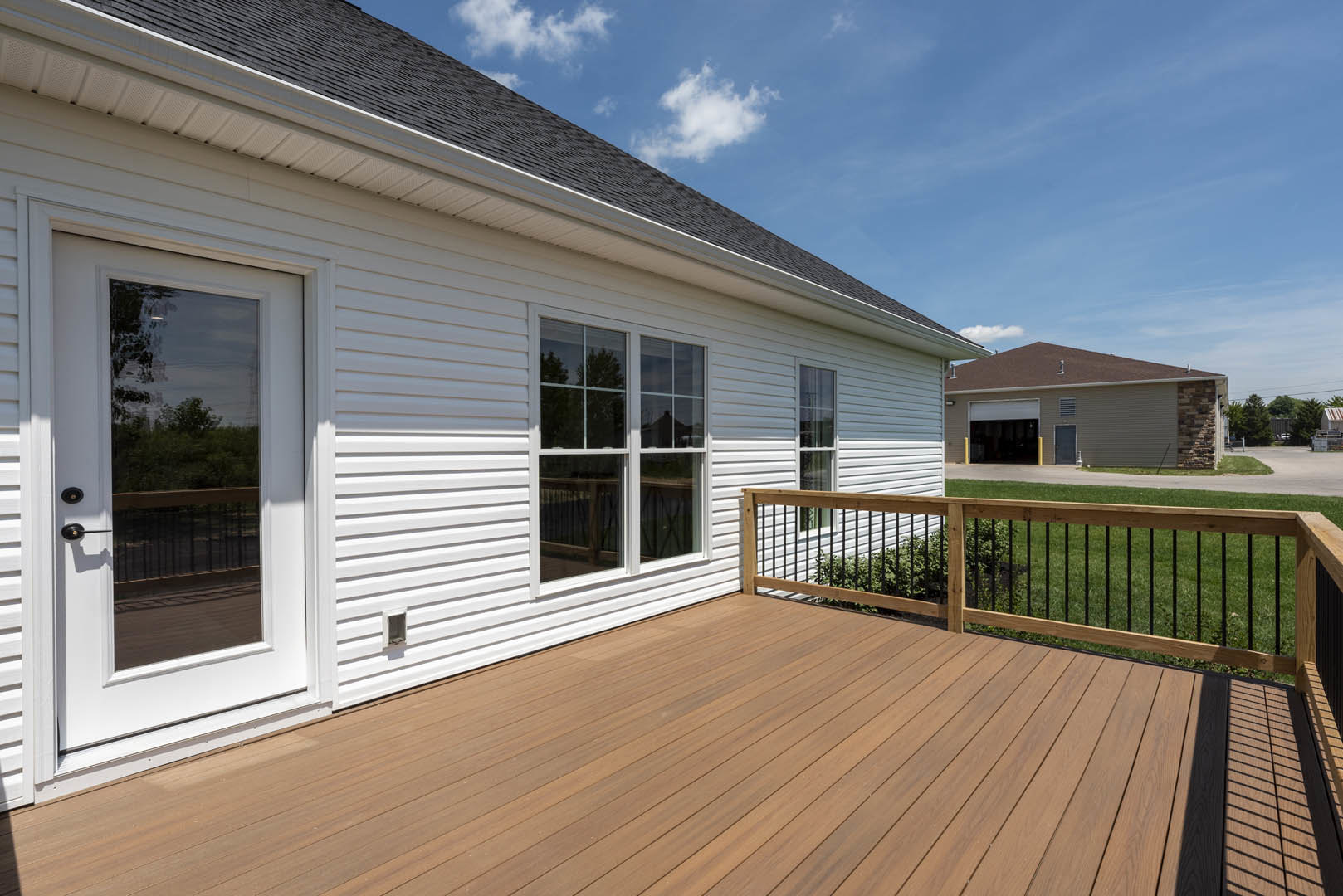 Wooden deck with horizontal railing, glass-paneled door, large window, and light-colored siding on house exterior