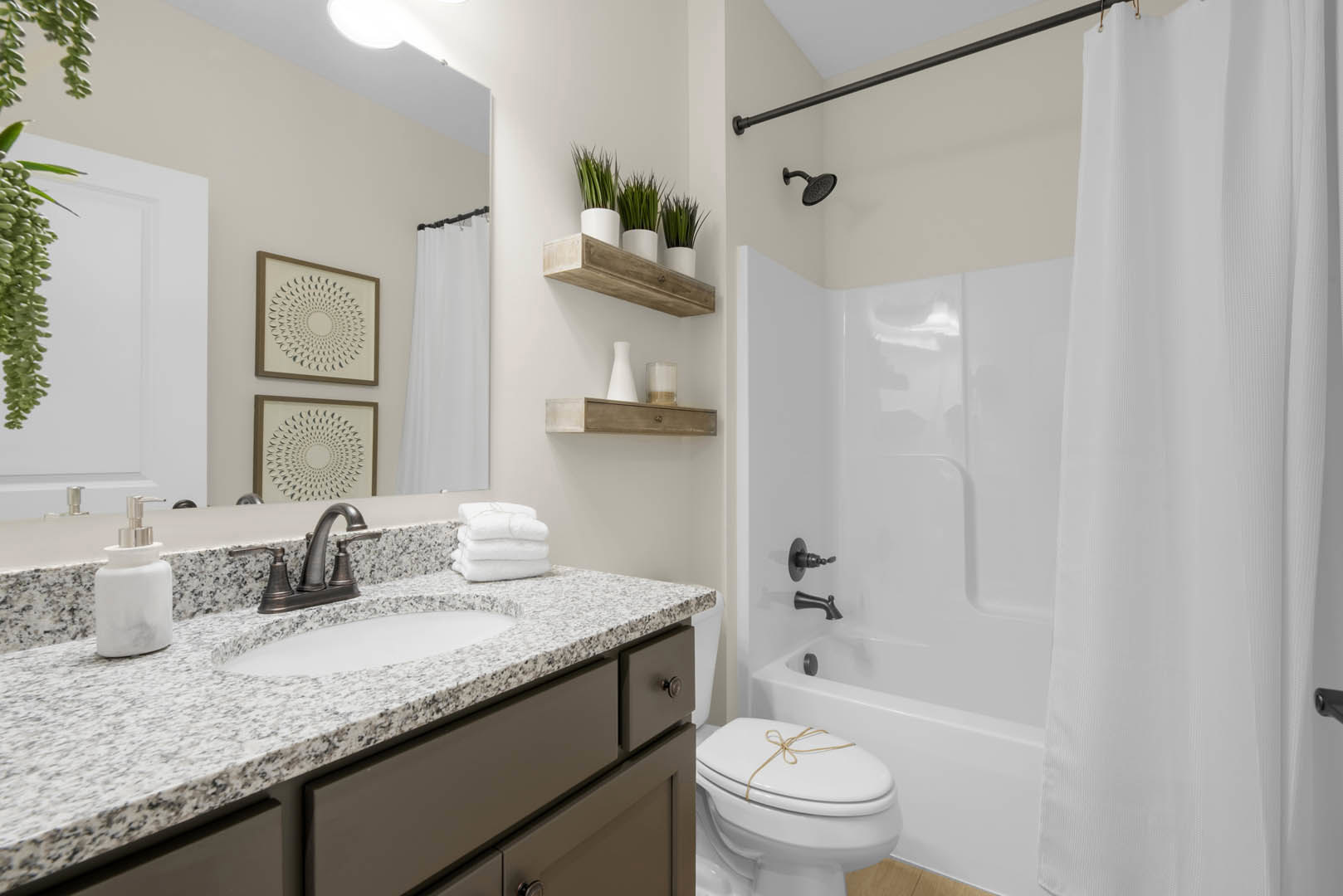 Modern bathroom featuring a tiled walk-in shower, white porcelain sink with chrome faucet, stacked white towels on a stone countertop, toilet with rope tied around lid, and framed