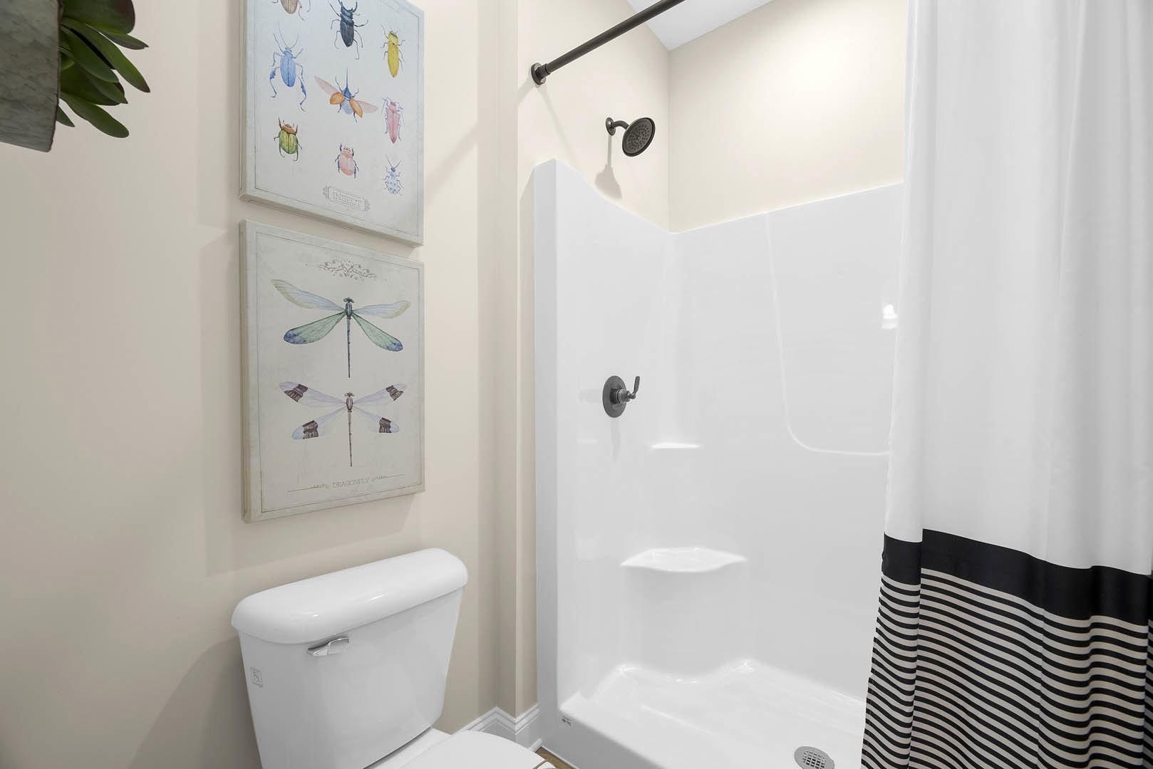 Modern bathroom with white tile walls, glass-enclosed shower, chrome shower head, wall-mounted faucet, and a white toilet adjacent to a painted artwork featuring insects