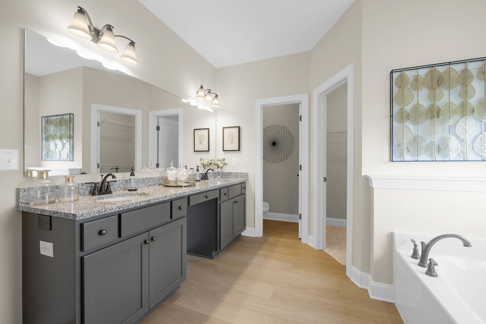 Bathroom with marble countertop, freestanding bathtub, decorative metal leaf wall art, framed pictures including a skull and a white object, three-light fixture, white electrical