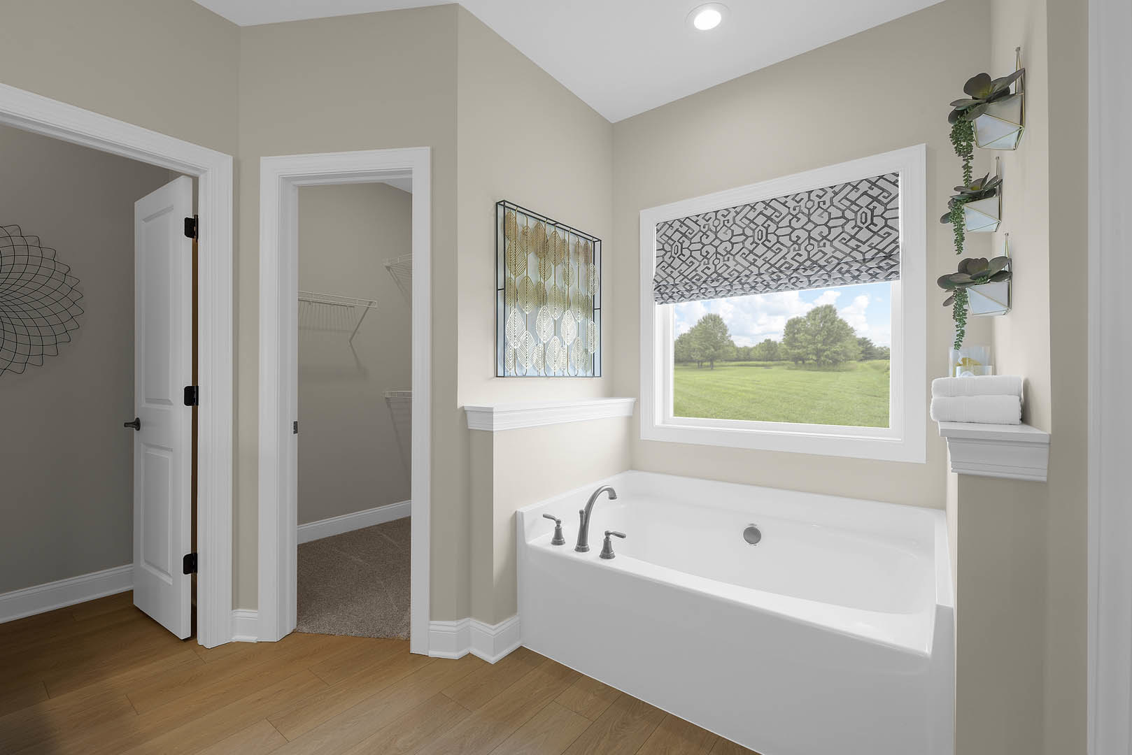 Freestanding bathtub with chrome faucets beneath patterned window, white door with black handle, light-colored walls and floor, wire mesh curtain partially visible