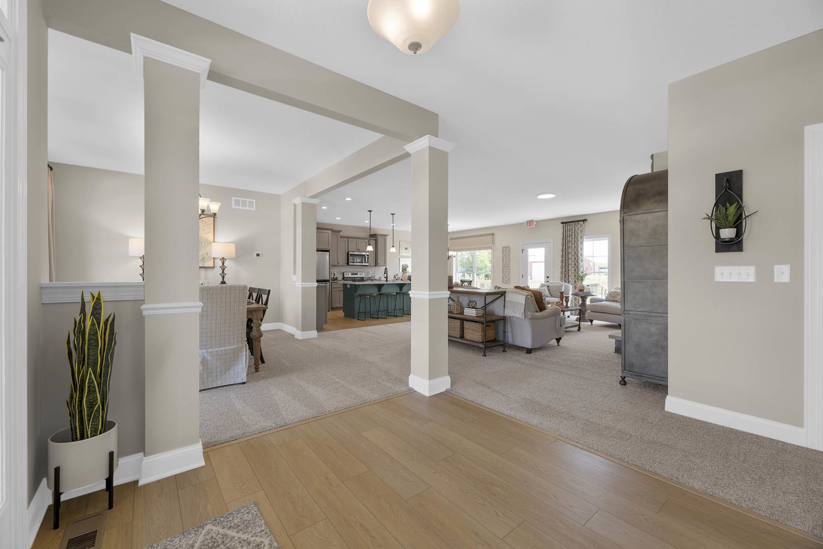 Spacious living room with wood laminate flooring, white plaster walls, recessed lighting, potted plants, built-in shelving with baskets and books, and an open layout extending into