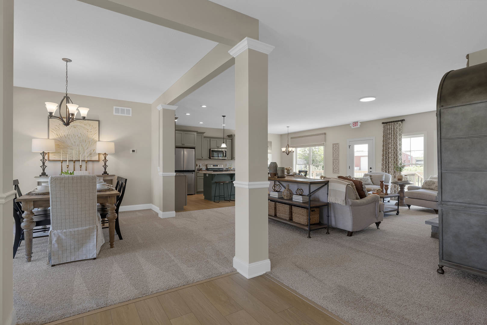 Open-concept living room and kitchen with light wood flooring, grey and white walls, white cabinetry, dining table, neutral-toned couch, and shelving with baskets and books