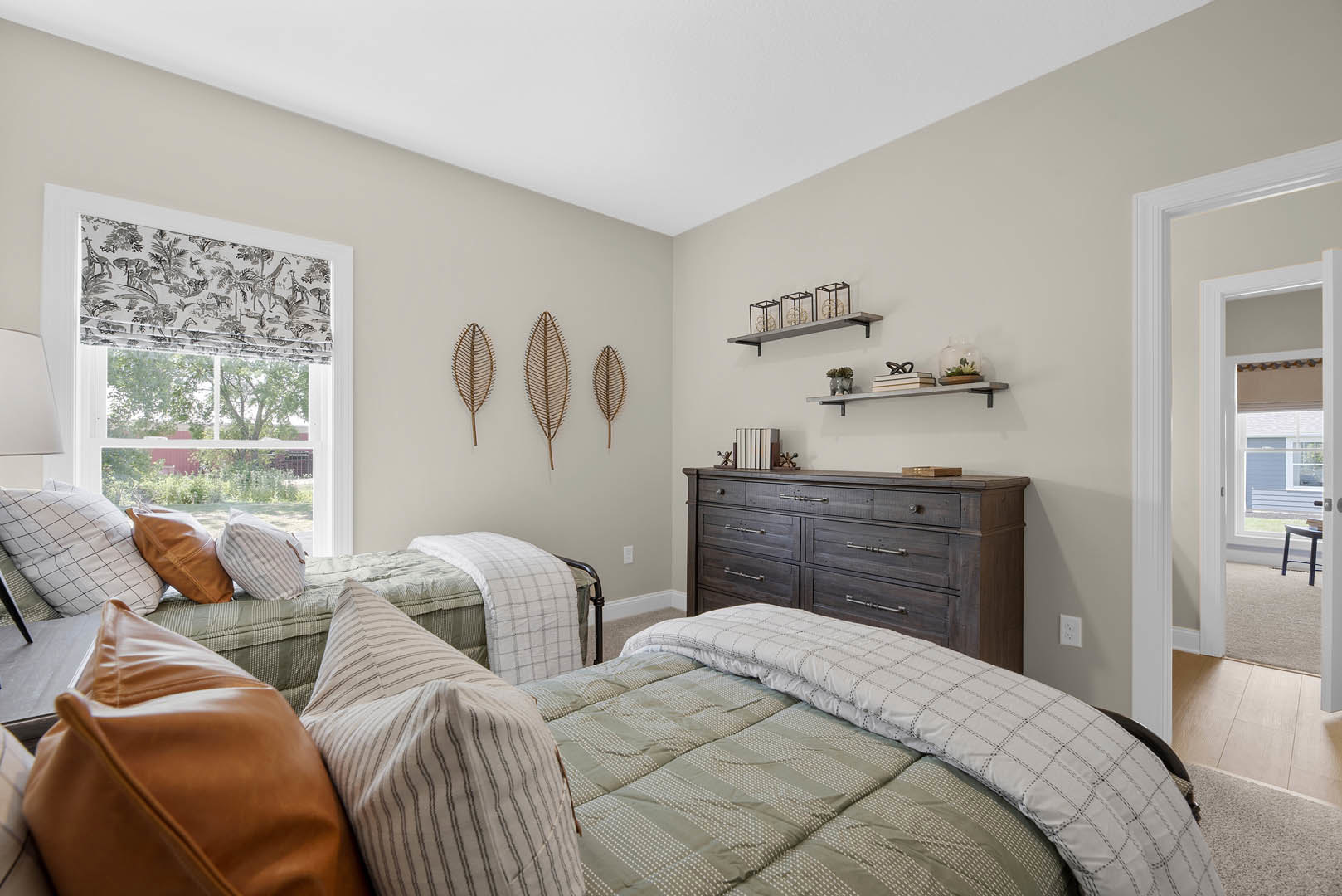 Bedroom with two twin beds featuring white linens and brown accent pillows, brown wooden dresser with drawers against a light-colored wall, neutral decor and soft lighting.
