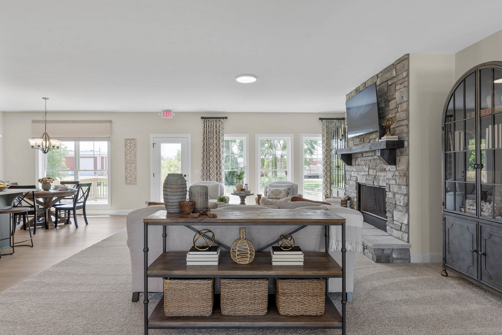 Living room with stone fireplace, light gray couch, built-in shelf holding baskets and decor, glass door with window, hardwood floors, close-up views of ceramic vase, woven basket