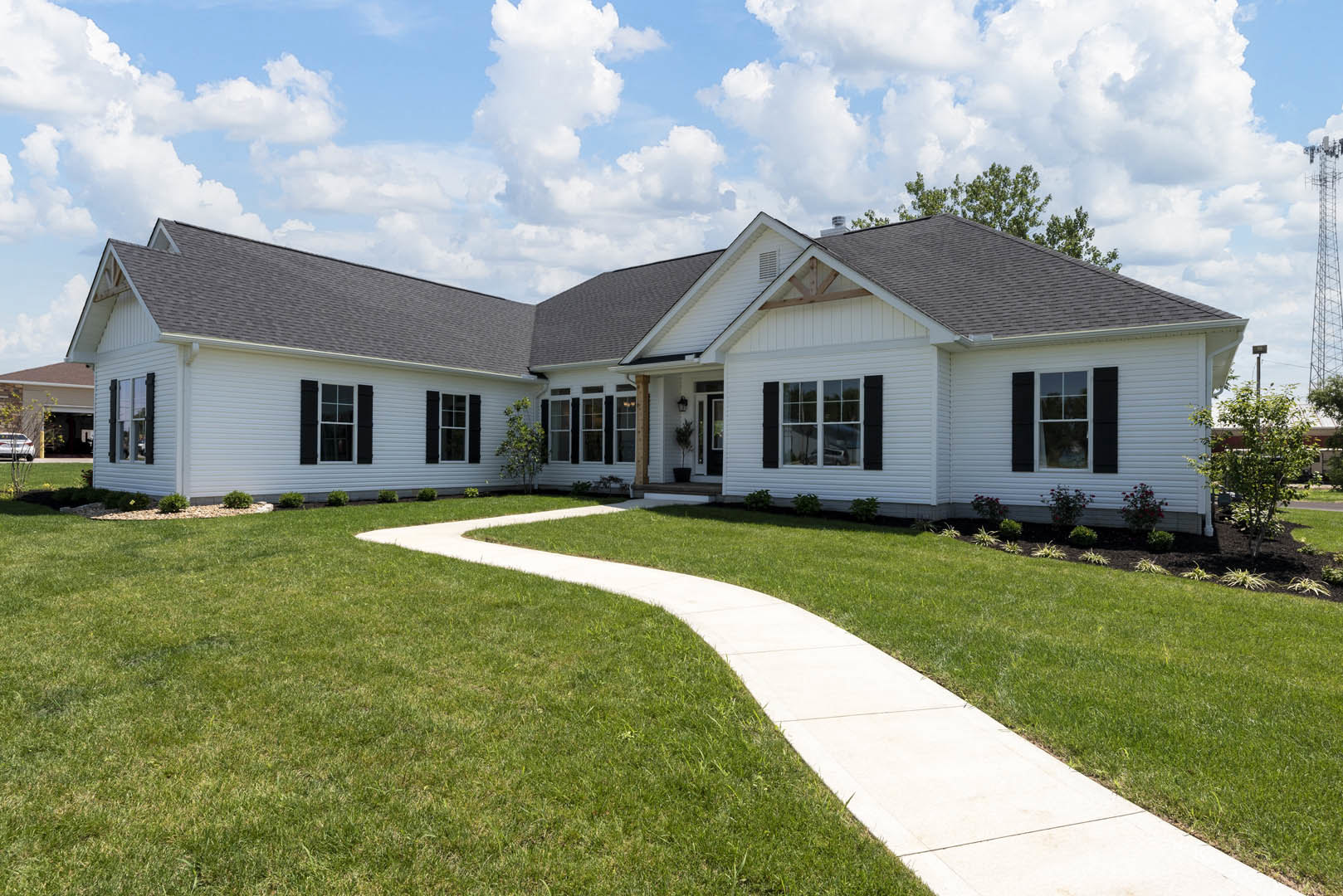 White siding house with black shuttered windows, covered front porch, green lawn, concrete walkway, and cloudy sky overhead