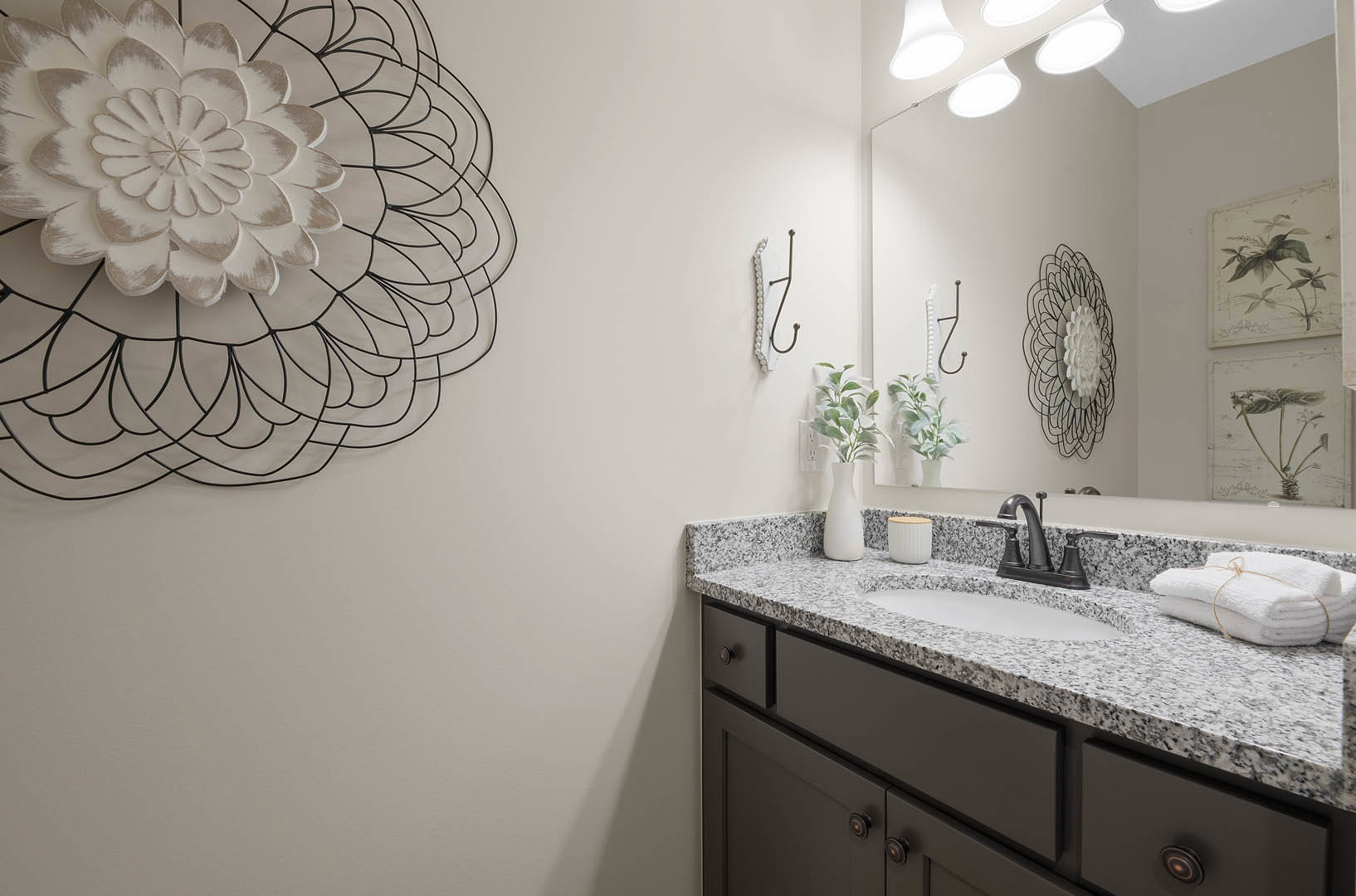 Modern bathroom with white sink and chrome faucet set in light wood cabinetry, rectangular mirror above, stack of white towels tied with rope, white container with wooden lid, and
