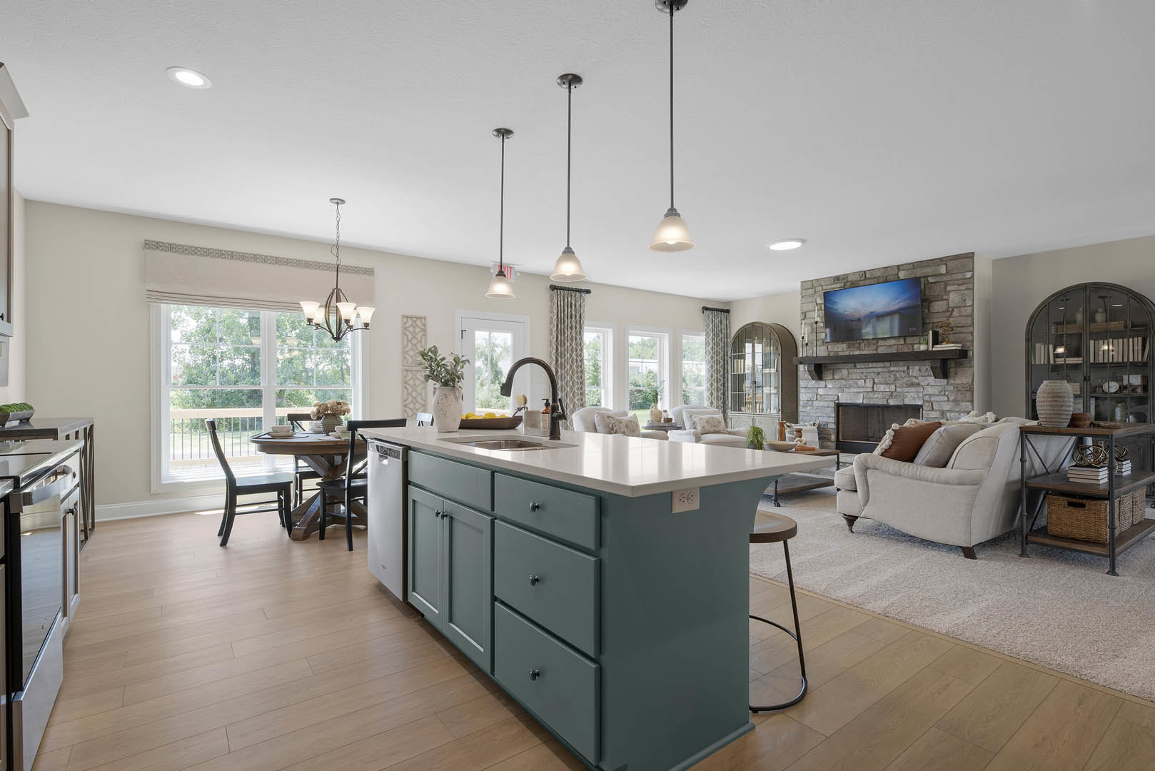 Open-concept kitchen and living room featuring a white countertop island with sink, light cabinetry, hardwood floors, modern fireplace, and contemporary furniture including a couch