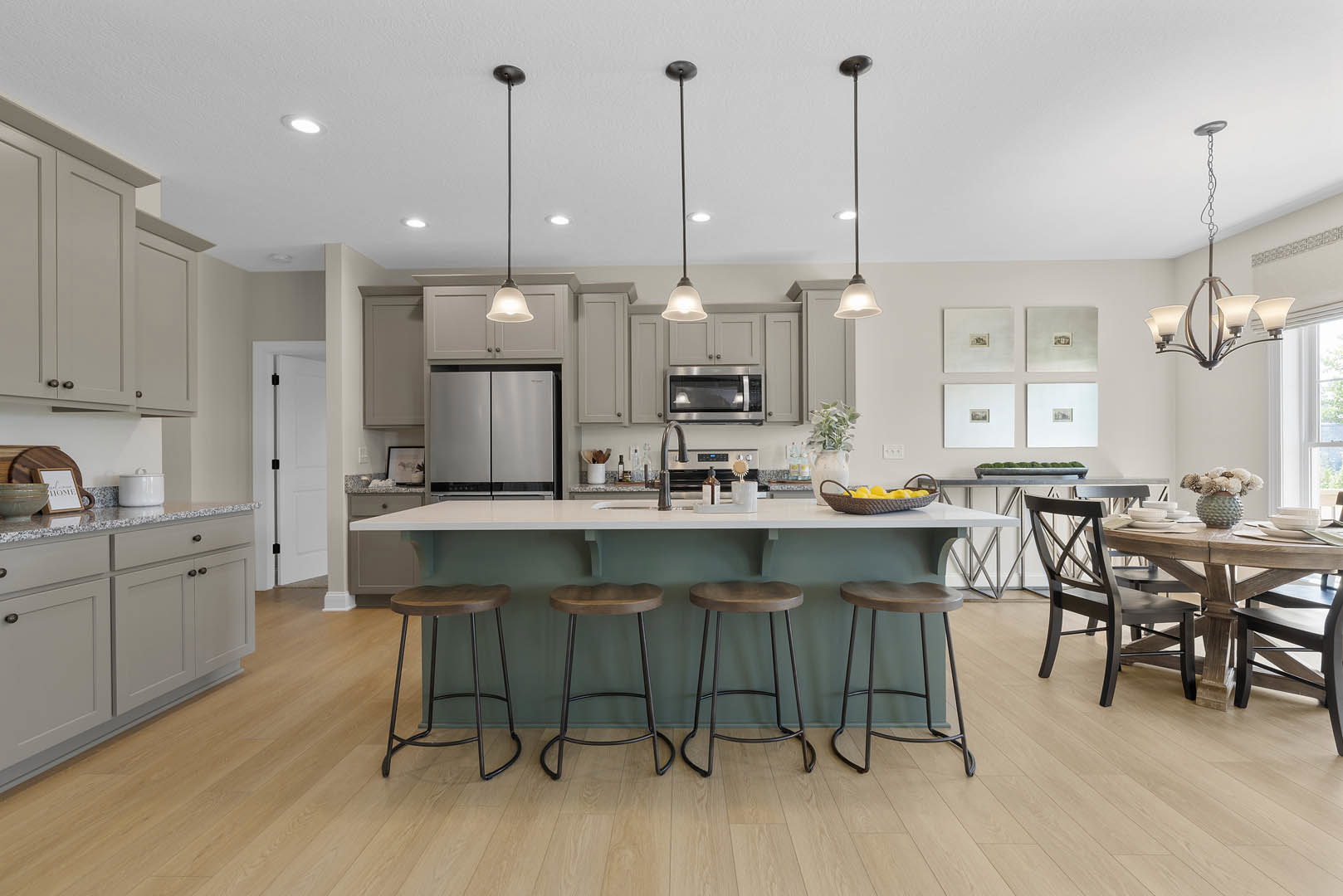 Modern kitchen with white cabinetry, central island featuring two wooden stools, dining table, stainless steel microwave, white refrigerator, and white pot on quartz countertop