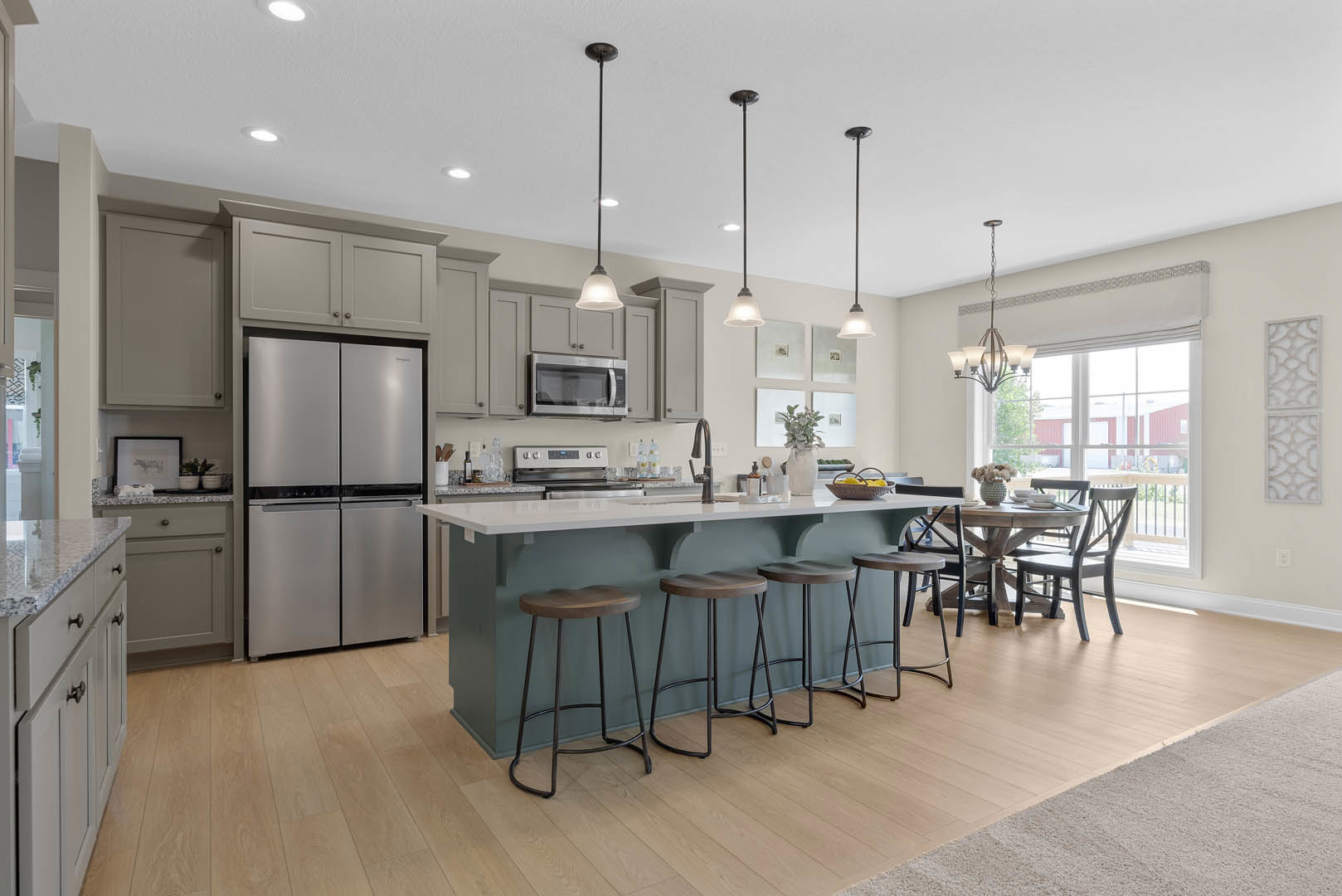 Spacious kitchen featuring a large central island with stone countertop, adjacent dining table, stainless steel refrigerator, glass-door microwave, wooden stools, white cabinetry