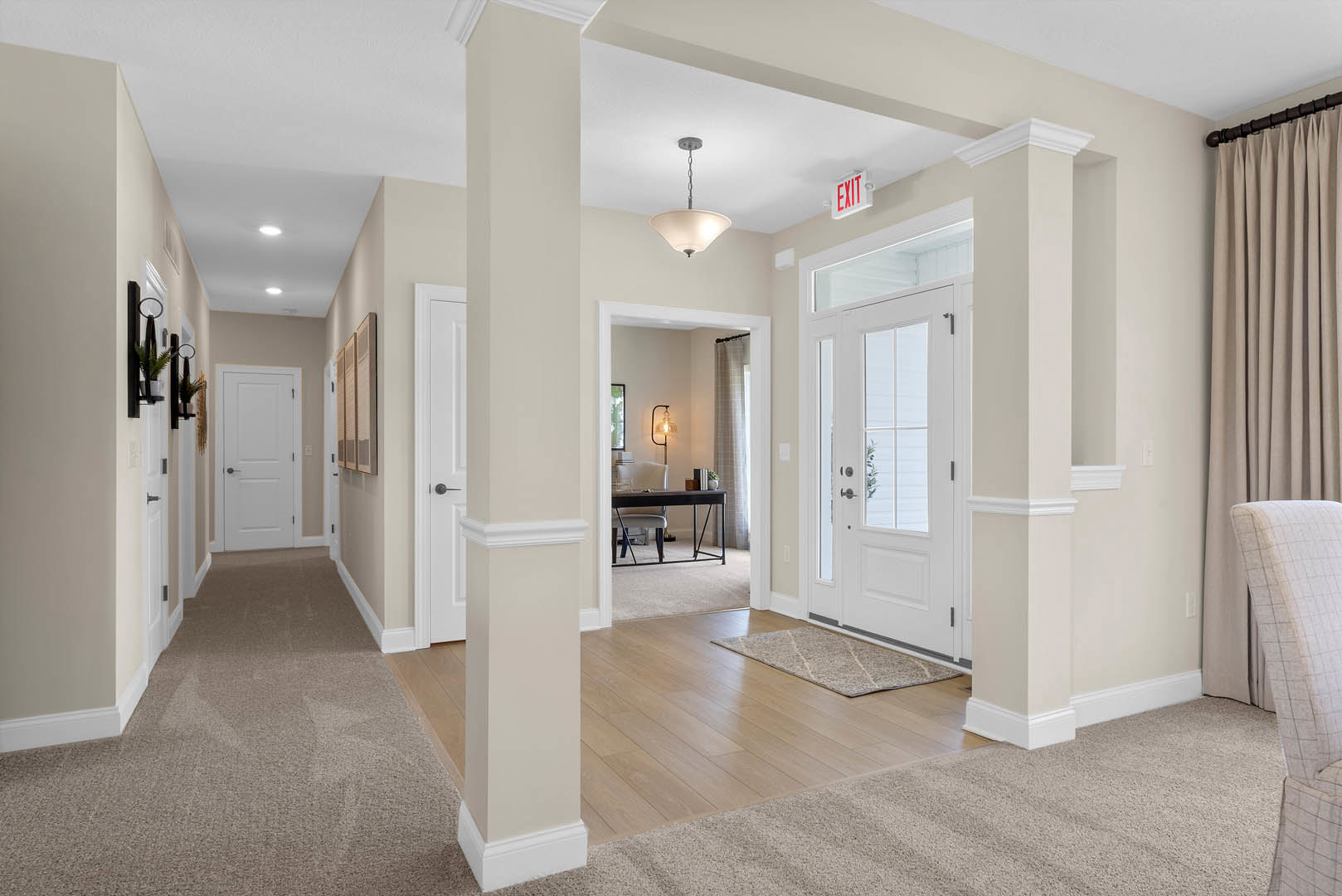 Hallway with white pillars, laminate wood flooring, white door with black handle, ceiling light fixture, desk with chair, white sign with red text, close-up of curtain