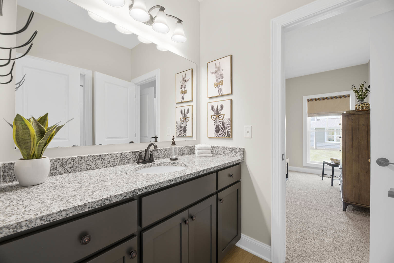 Bathroom with marble countertop, white cabinetry, black hardware, potted plant, and modern faucet