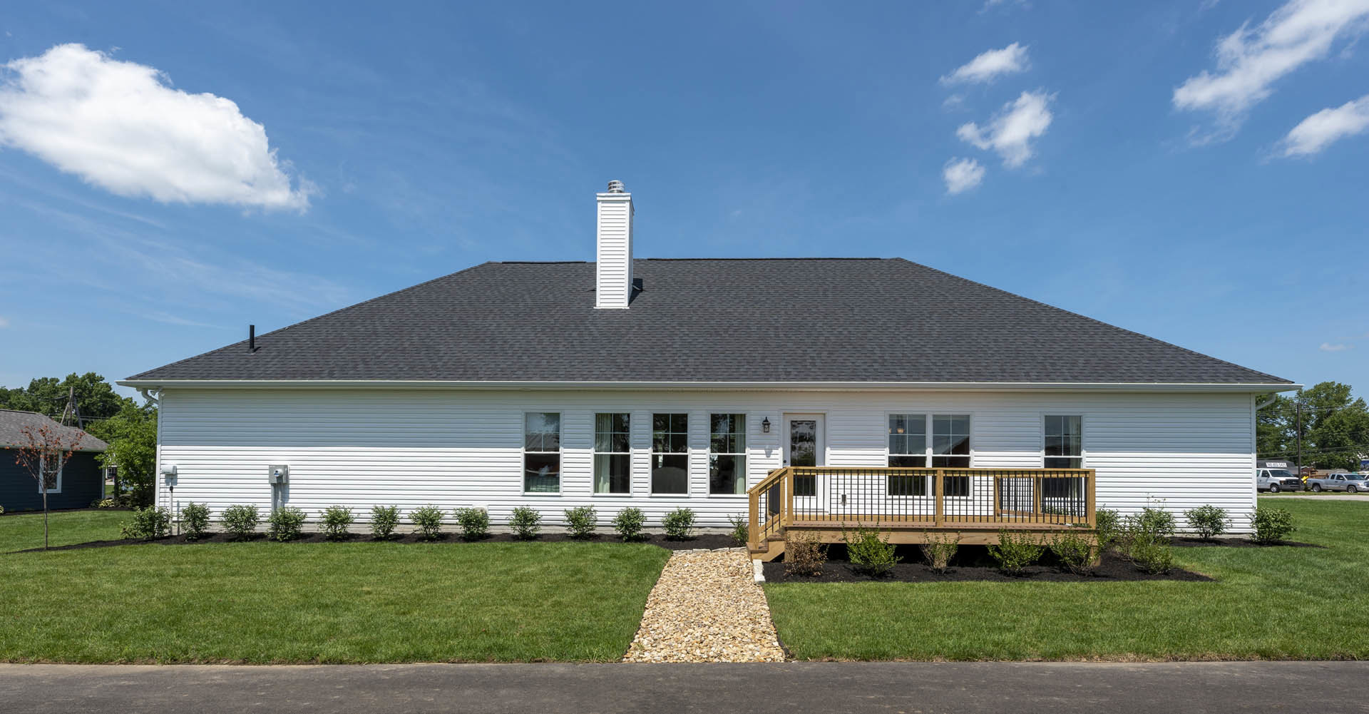 Modern house with wood deck, gravel walkway bordered by grass, large windows, and blue sky overhead