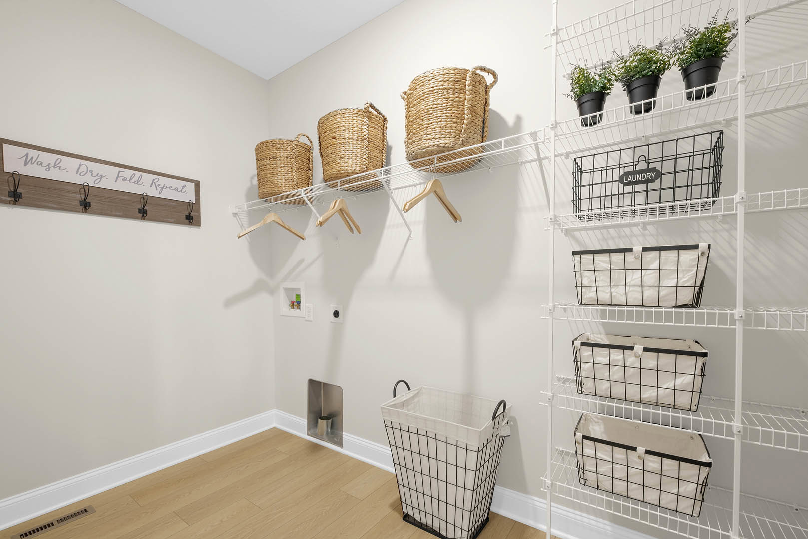 White wire baskets and black clothes racks mounted on a wall grid in a laundry room, with a black sign and light-colored flooring visible.