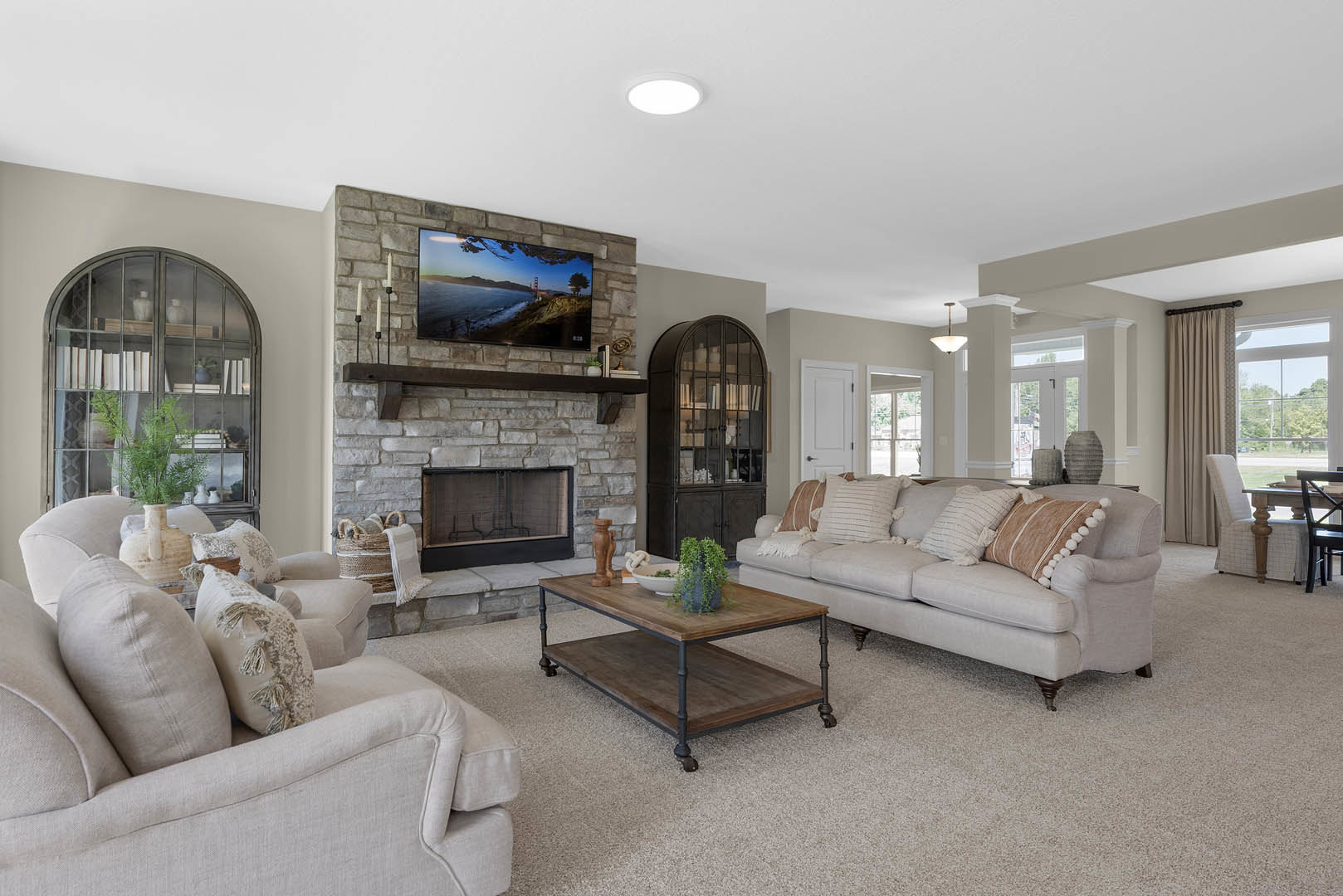 Living room with neutral couches, decorative pillows, central fireplace with white mantel, coffee table topped with a potted plant, side table holding a vase, framed beach and