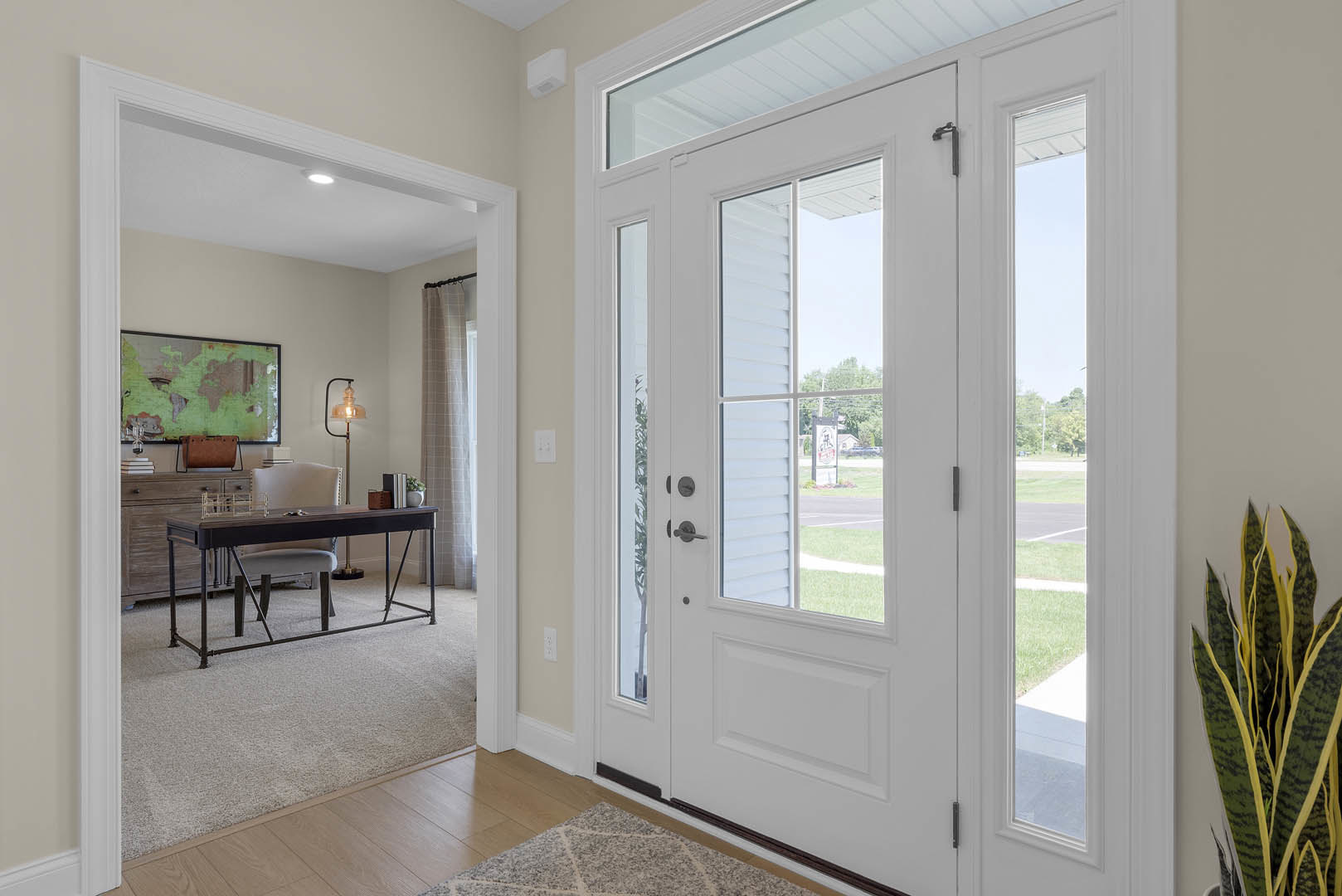 White double doors with glass panes set in a light-colored wall, hardwood flooring, a houseplant in a vase, a chair tucked under a table, and a world map artwork displayed nearby.