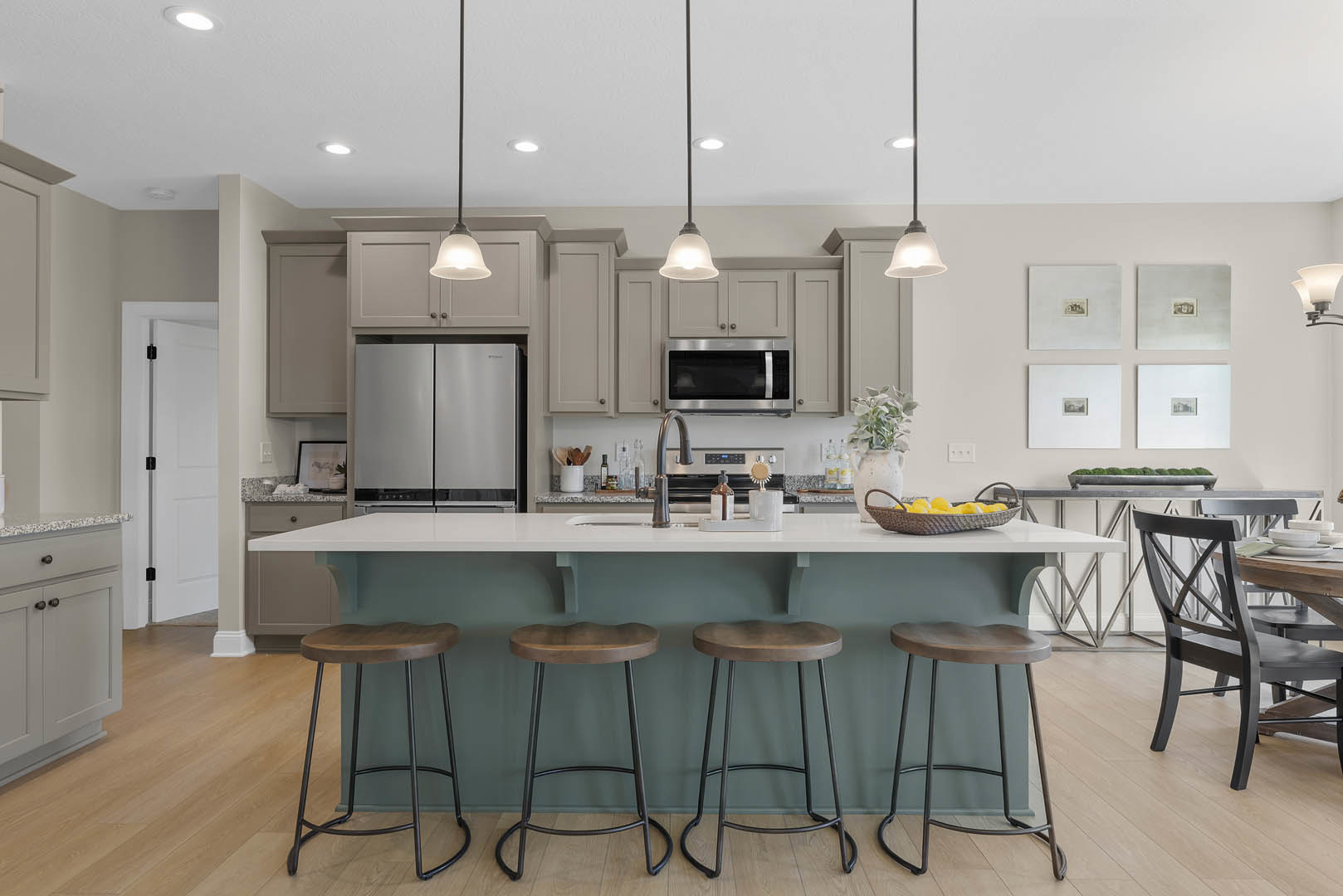 Modern kitchen featuring a central island with two wooden seat stools, white cabinetry, black-handled refrigerator, built-in microwave, light countertops, and hardwood flooring.