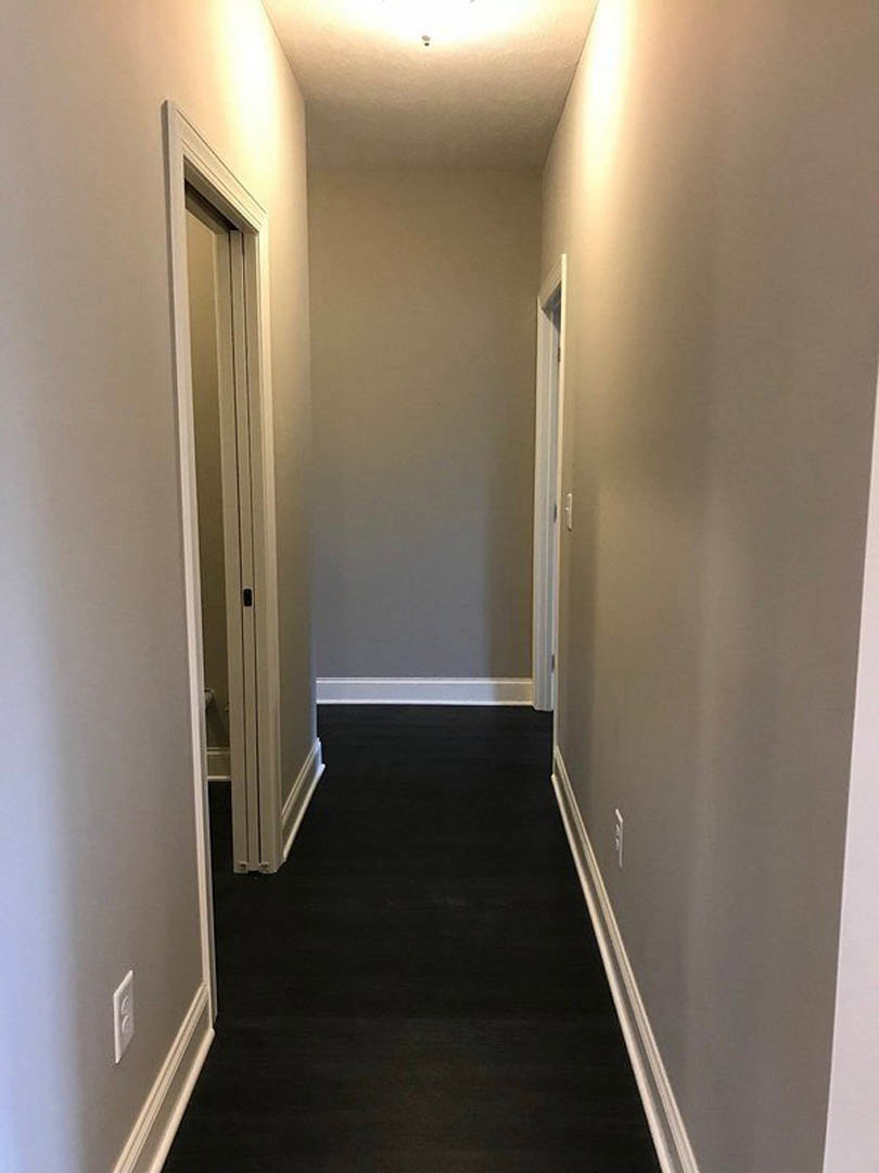 Hallway with white walls, white door, black flooring, white trim, and wall-mounted light fixture