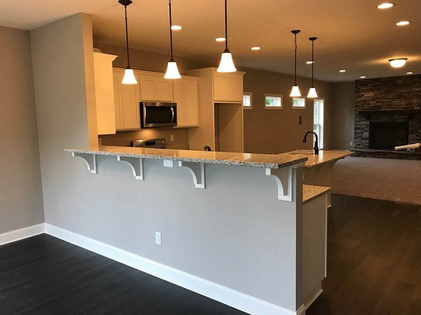 Open-concept kitchen and living room featuring a stone fireplace, wood cabinetry, bar seating at a quartz countertop, stainless steel microwave, modern ceiling fixtures, and a