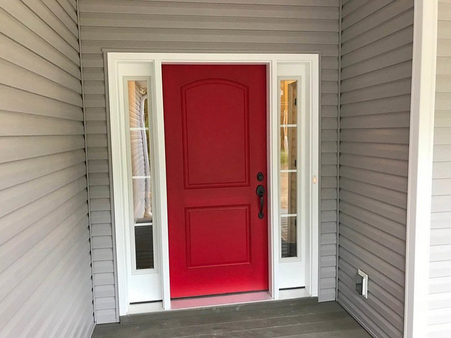 Red front door with white trim and black handles set in grey exterior wall