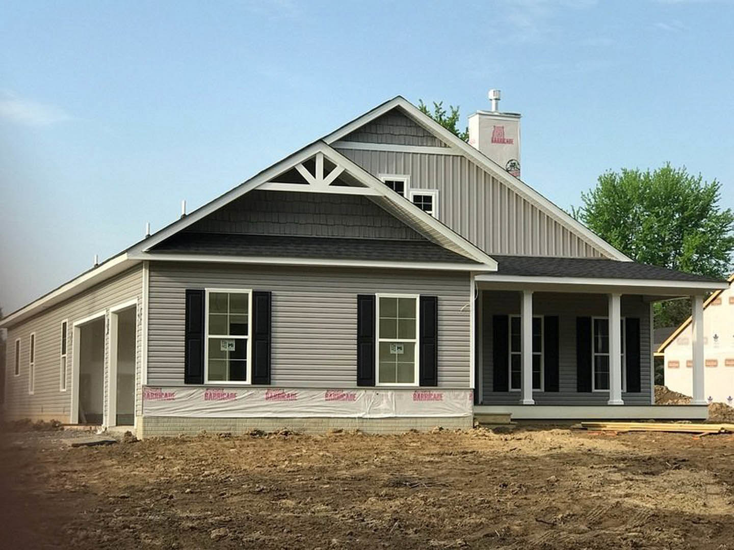 Wood-framed house under construction with exposed chimney, open door, and window displaying a sign; dirt lot and leafy trees surround the site, Palm Cottage visible in the