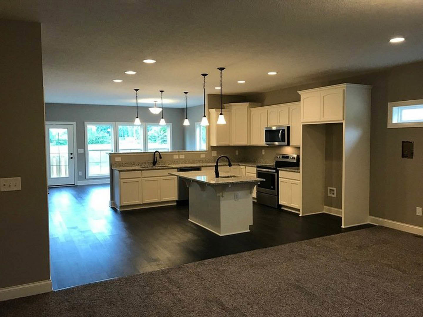 Open-concept kitchen and living room featuring a spacious white island with black accents, modern cabinetry, black curved faucet, built-in microwave, light wood flooring, and