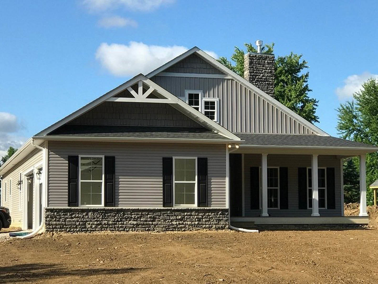 Brick house with black shuttered windows, white window frames, prominent chimney, and a dirt yard bordered by a stone wall
