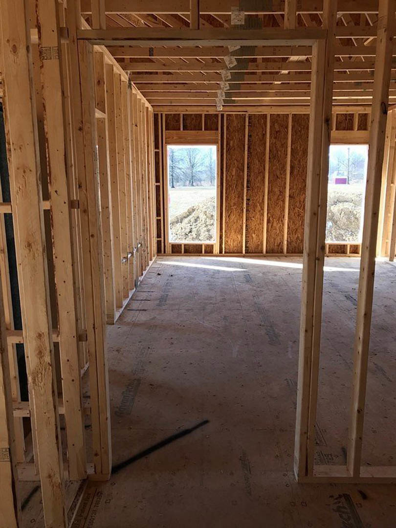 Unfinished room with exposed wood framing, large window overlooking snowy trees, construction materials and insulation visible