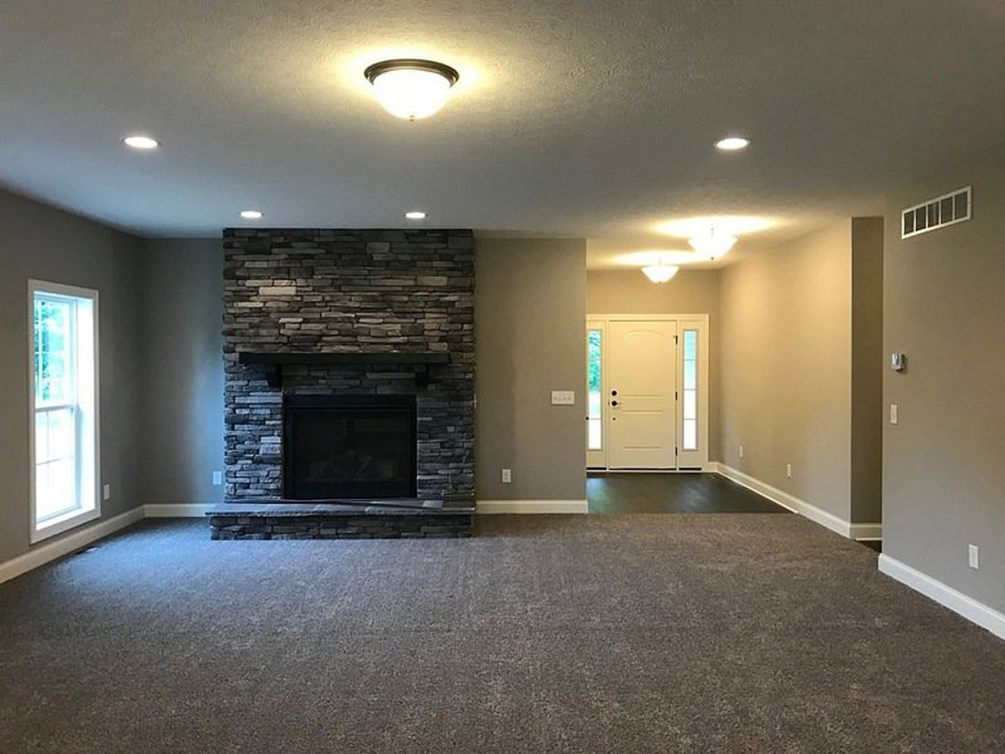 Carpeted living room featuring a stone fireplace, white door with glass windows, plaster walls, and ceiling