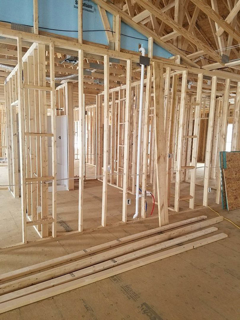 Exposed wood framing and beams in a residential home under construction, with natural brown lumber and unfinished surfaces visible.