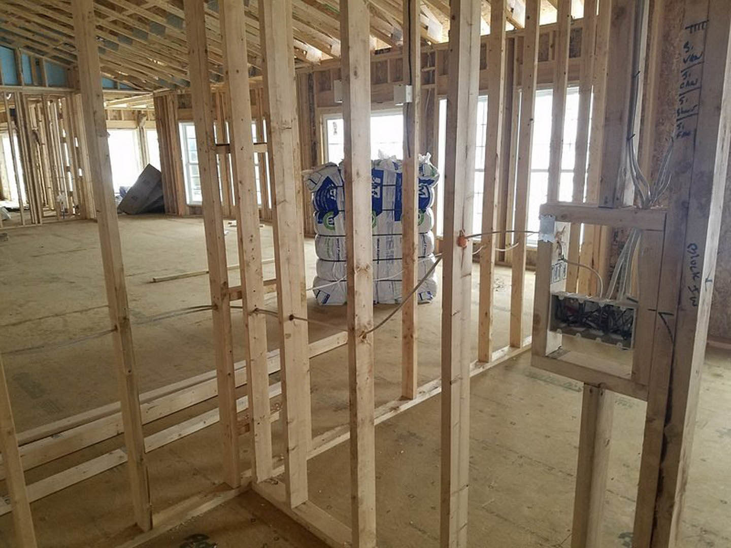 Unfinished room with exposed wood framing, electrical wiring, and a stack of white bags on the floor near a window