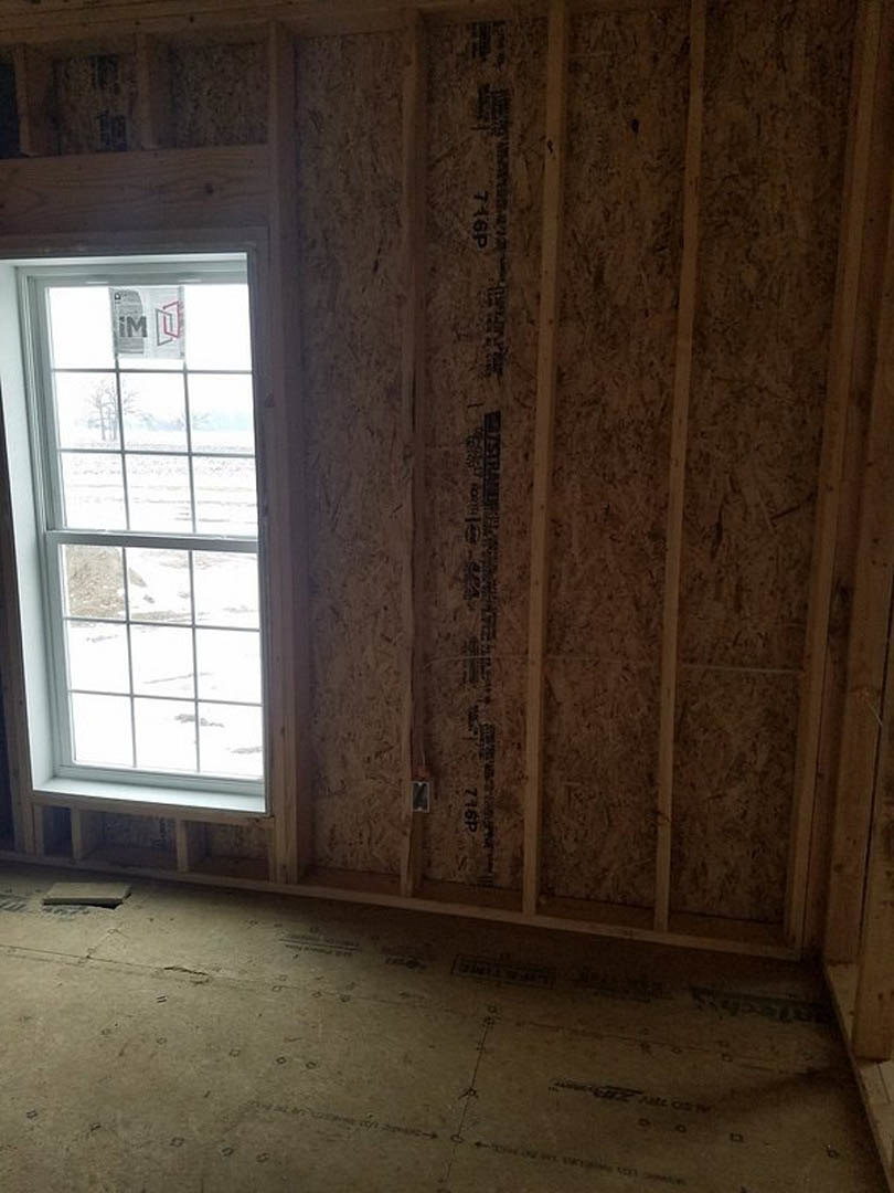 Large window framed by wood paneling in a room, offering a view of a snowy field; light-colored plaster walls and hardwood flooring visible.