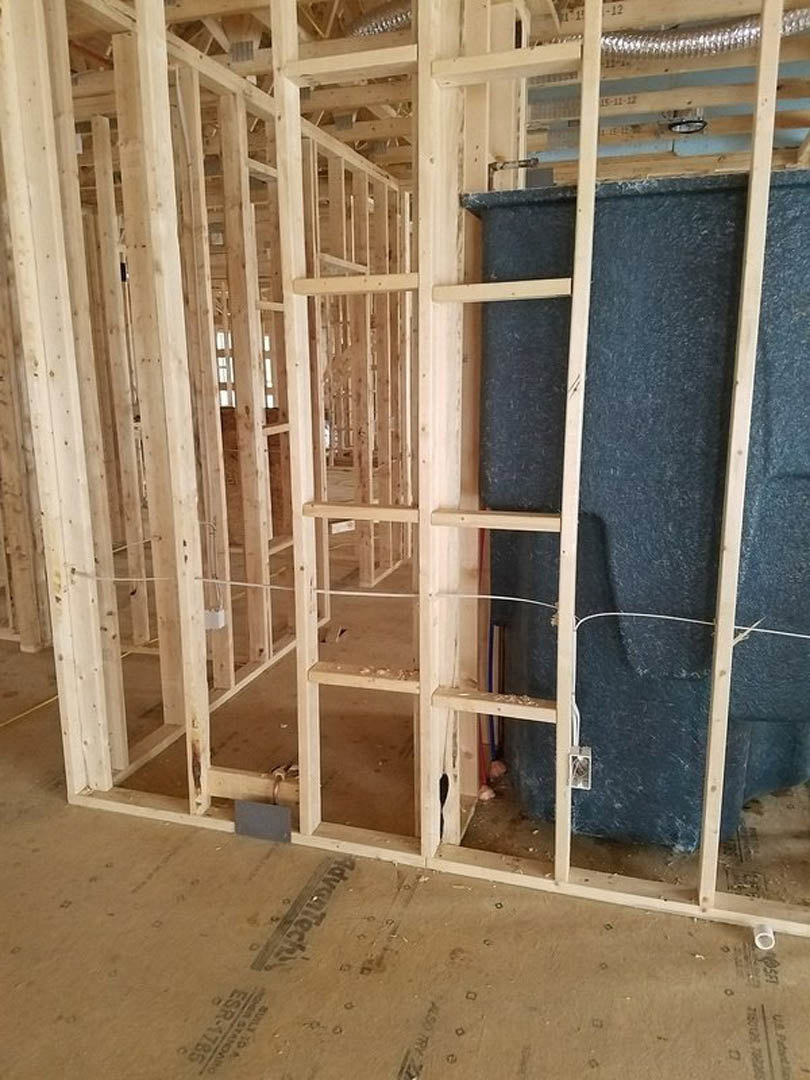 Exposed wooden framing with blue insulation panels, unfinished interior walls, metal ladder, and construction materials in a residential build.
