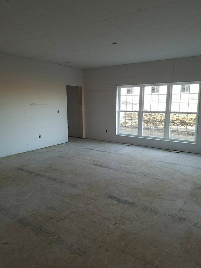 Spacious room featuring a large window framed by a stone accent wall, white plaster walls with black trim, light-colored flooring, and ceiling fixtures; person standing near the
