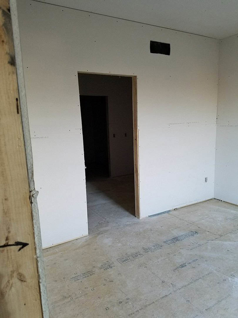 Concrete floor and plaster walls in a dimly lit room, open door revealing wood trim and black screen with white frame on adjacent surface