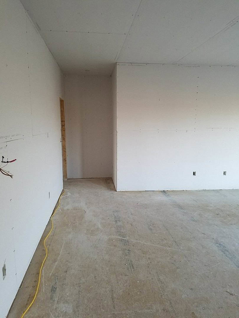 White plaster wall with exposed yellow wire, unfinished concrete floor, and partial wooden framing visible along the base.