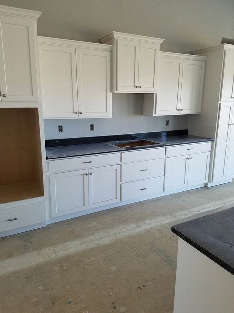 White kitchen cabinets with black countertops, stainless steel appliances, brown accent wall, and white door.