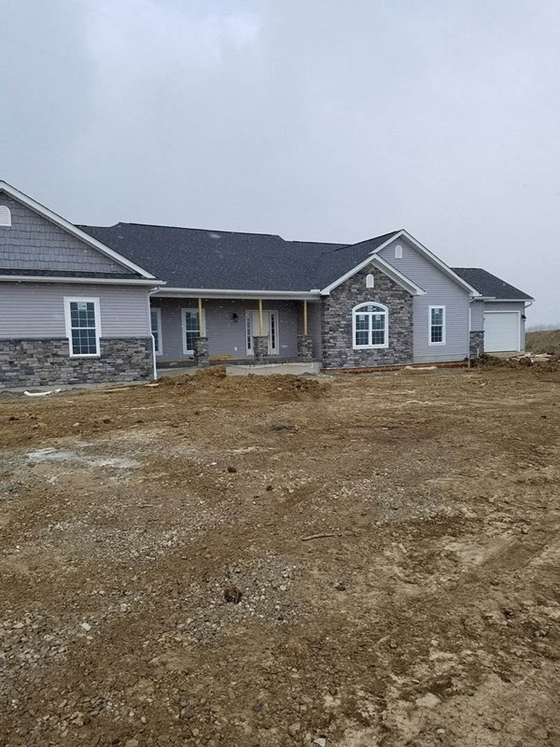Two-story house with grey roof, white garage door, brick exterior walls, white-framed windows, and a dirt field in front