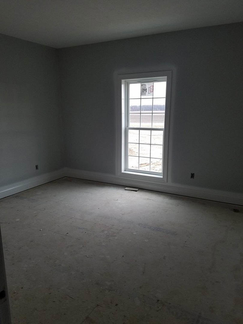 Bright room with white plaster walls, large window offering outdoor view, light wood flooring, and a small hole in the floor near the window.