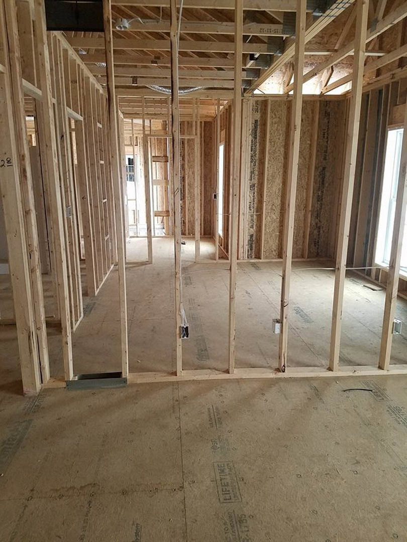 Wood-framed room with exposed beams, unfinished floor, window letting in natural light, visible stone detail and metal grate