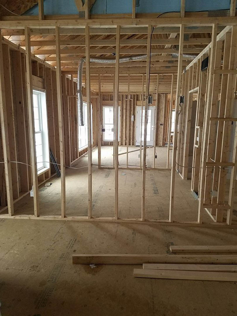Wood-framed room under construction with exposed beams, unfinished walls, and daylight streaming through a large window