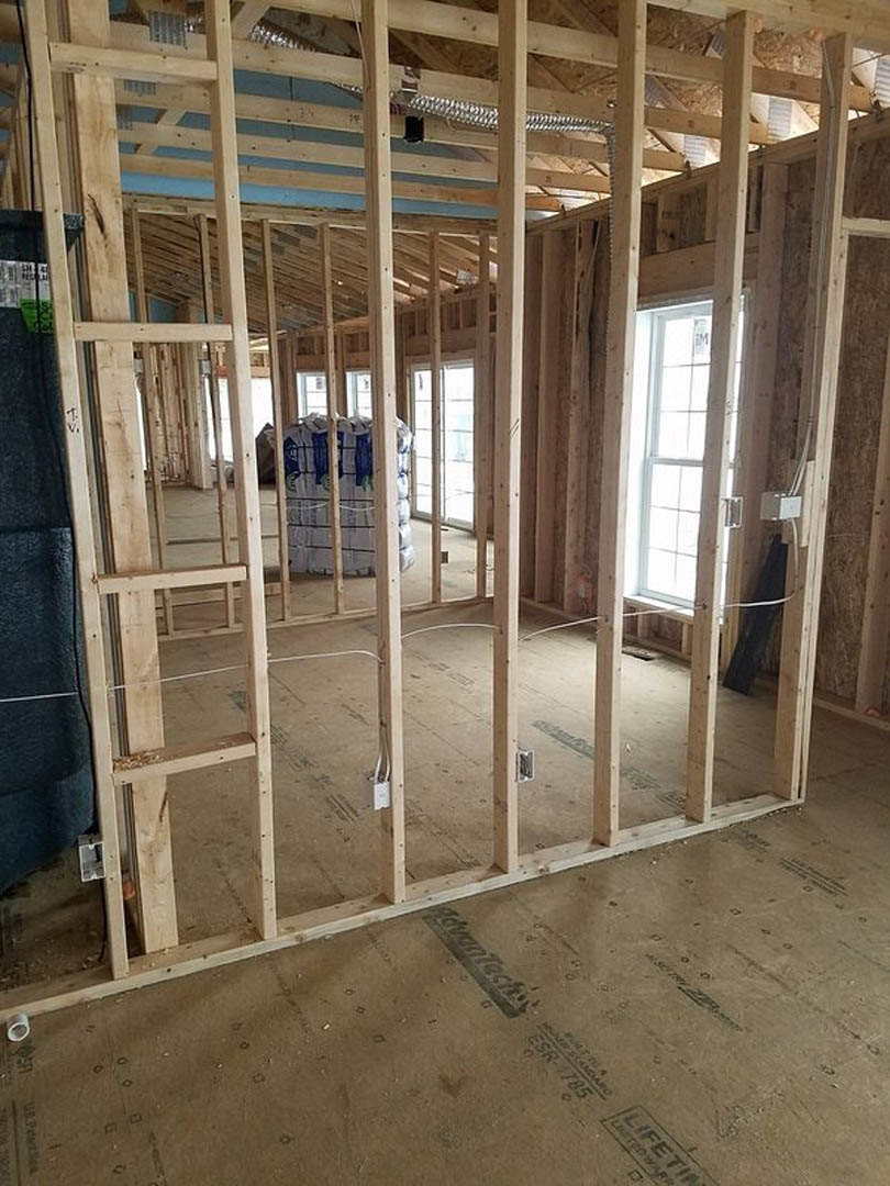 Exposed wood framing and beams inside a partially constructed home with unfinished concrete floor and white-framed window