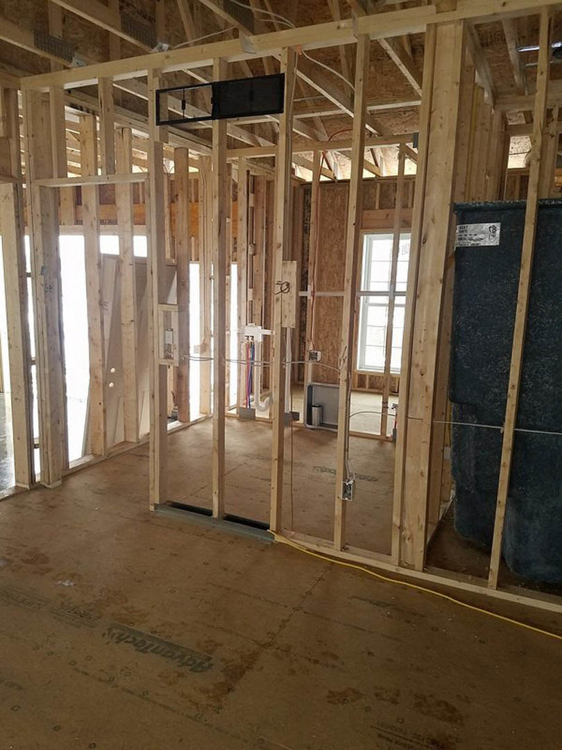 Unfinished room featuring exposed wood framing, wooden planks along the wall, black rectangular object with wooden trim, wood framing on the floor, and a window with a white frame.