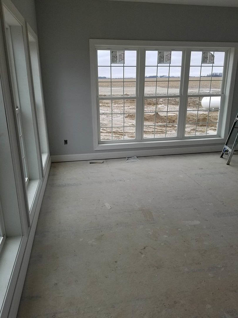 Spacious room featuring a large window overlooking a grassy field, polished concrete floor, white plaster walls, and modern black-accented light fixture.