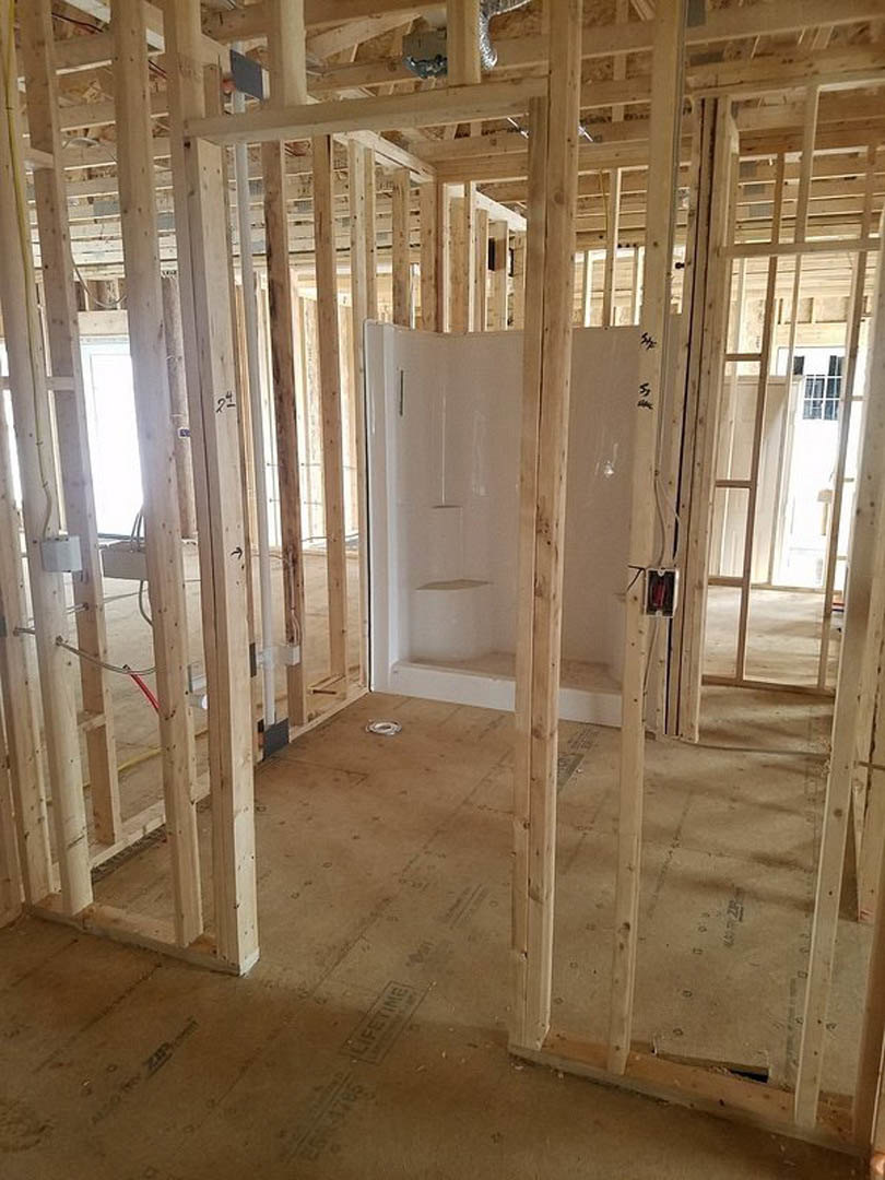 Bathroom under construction with exposed wood framing, white shower stall, unfinished walls, door, and windows.