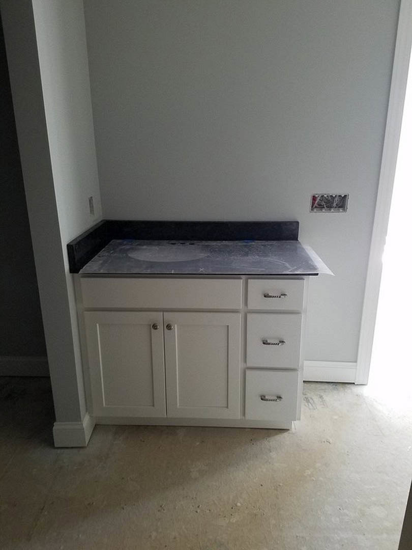 White kitchen countertop with built-in drawers, grey tile floor, and light cabinetry.