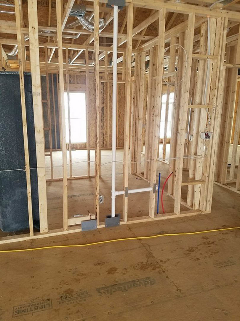 Exposed wood framing with beams and planks, yellow electrical cable on subfloor, white wall featuring a window, brown surface detail, construction sign visible in foreground