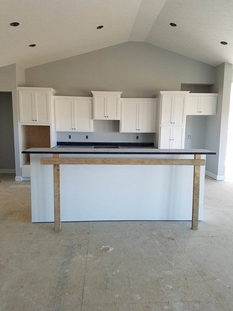 Kitchen with white shaker cabinets, silver handles, light stone countertops, stainless steel sink, grey accent wall, and wood-framed whiteboard