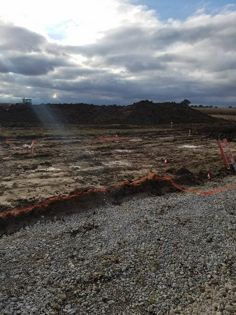 Dirt field with scattered ladders under a cloudy sky, rocky ground with red streaks, outdoor landscape