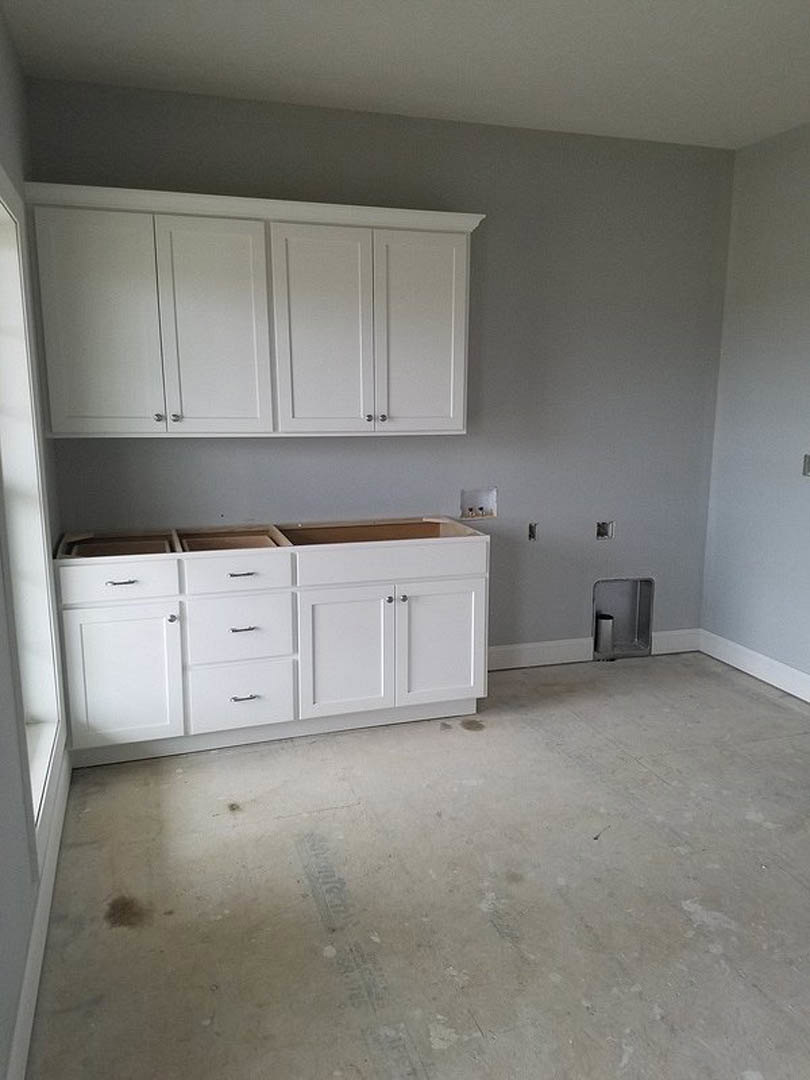 White kitchen with shaker-style cabinets, stainless steel sink, light stone countertops, and drawers beneath the counter.